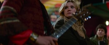 Movie still from “Zombieland: Double Tap” (2019), directed by Ruben Fleischer – A woman holding a guitar in front of another person; Close Up shot, Over the shoulder angle