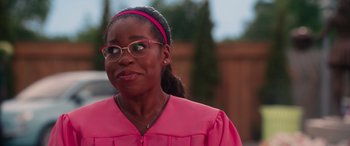 Movie still from “Zombies 3” (2022), directed by Paul Hoen – A woman in a pink graduation gown and glasses; Close Up shot, Over the shoulder angle