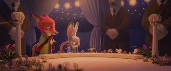 Movie still from “Zootopia” (2016), directed by Jared Bush – A group of animals sitting on top of a wooden table; Medium shot, Over the shoulder angle