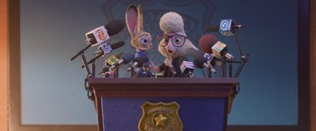Movie still from “Zootopia” (2016), directed by Jared Bush – A couple of people that are sitting at a podium; Medium shot, Low angle
