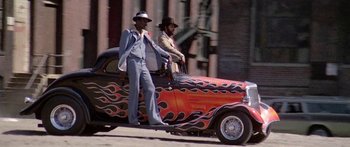 Movie still from “1990: The Bronx Warriors” (1982), directed by Enzo G. Castellari – Two men are standing on the hood of an antique car; Wide shot, Low angle