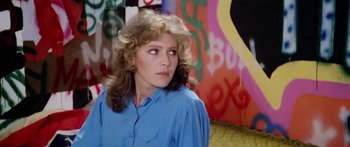 Movie still from “1990: The Bronx Warriors” (1982), directed by Enzo G. Castellari – A woman in a blue shirt is standing in front of a wall; Close Up shot, Over the shoulder angle