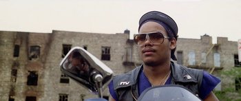 Movie still from “1990: The Bronx Warriors” (1982), directed by Enzo G. Castellari – A man wearing sunglasses and a hat on a moped; Close Up shot, Low angle