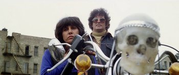 Movie still from “1990: The Bronx Warriors” (1982), directed by Enzo G. Castellari – A man and a woman are standing on a motorcycle; Medium shot, Low angle