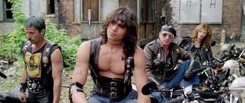 Movie still from “1990: The Bronx Warriors” (1982), directed by Enzo G. Castellari – A man in a leather vest sitting next to another man; Medium shot, Low angle