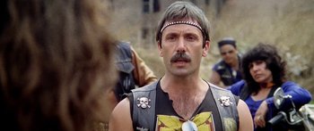Movie still from “1990: The Bronx Warriors” (1982), directed by Enzo G. Castellari – A man with a beard and mustache wearing a leather vest; Close Up shot, Over the shoulder angle