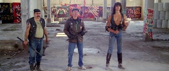Movie still from “1990: The Bronx Warriors” (1982), directed by Enzo G. Castellari – A man standing next to another man holding a gun; Wide shot, Low angle