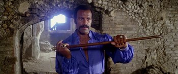 Movie still from “1990: The Bronx Warriors” (1982), directed by Enzo G. Castellari – A man holding a wooden stick in his hands; Medium shot, Low angle