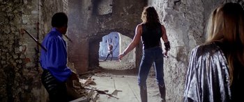 Movie still from “1990: The Bronx Warriors” (1982), directed by Enzo G. Castellari – A man in a black shirt is holding a knife; Wide shot, Over the shoulder angle