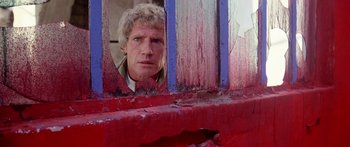 Movie still from “1990: The Bronx Warriors” (1982), directed by Enzo G. Castellari – A man looking out a window through a red fence; Close Up shot, Low angle