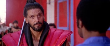 Movie still from “1990: The Bronx Warriors” (1982), directed by Enzo G. Castellari – A person with a beard wearing a vest; Close Up shot, Over the shoulder angle