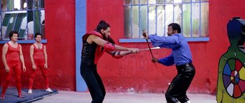 Movie still from “1990: The Bronx Warriors” (1982), directed by Enzo G. Castellari – Two men are fighting with swords in front of a red wall; Medium shot, Over the shoulder angle