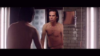 Movie still from “20,000 Days on Earth” (2014), directed by Iain Forsyth – A man looking at himself in the mirror in front of a mirror; Medium shot, Over the shoulder angle
