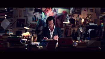 Movie still from “20,000 Days on Earth” (2014), directed by Iain Forsyth – A man sitting at a desk in front of a laptop computer; Medium shot, High angle