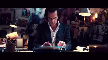 Movie still from “20,000 Days on Earth” (2014), directed by Iain Forsyth – A man sitting at a table typing on a keyboard; Medium shot, High angle