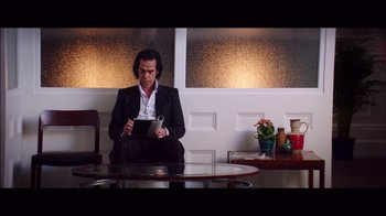 Movie still from “20,000 Days on Earth” (2014), directed by Iain Forsyth – A man sitting in a chair holding a tablet; Medium shot, Low angle