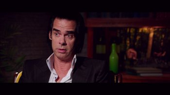 Movie still from “20,000 Days on Earth” (2014), directed by Iain Forsyth – A man sitting in a chair in front of a wine bottle; Close Up shot, Over the shoulder angle