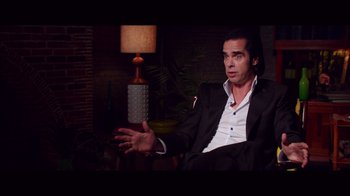 Movie still from “20,000 Days on Earth” (2014), directed by Iain Forsyth – A man in a suit sitting in front of a lamp; Medium shot, High angle