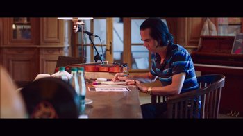 Movie still from “20,000 Days on Earth” (2014), directed by Iain Forsyth – A man sitting at a wooden table with a violin; Medium shot, High angle
