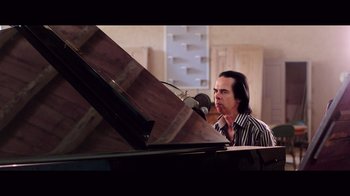 Movie still from “20,000 Days on Earth” (2014), directed by Iain Forsyth – A man sitting in front of a piano in front of a microphone; Medium shot, Low angle