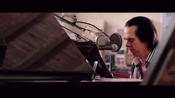 Movie still from “20,000 Days on Earth” (2014), directed by Iain Forsyth – A man with a microphone is playing a piano; Close Up shot, Low angle