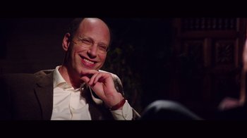 Movie still from “20,000 Days on Earth” (2014), directed by Iain Forsyth – A man with glasses smiles while holding his hand to his ear; Close Up shot, Over the shoulder angle