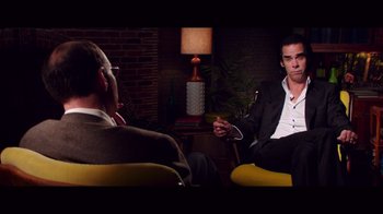 Movie still from “20,000 Days on Earth” (2014), directed by Iain Forsyth – A man in a suit sitting in front of another man in a suit; Medium shot, Over the shoulder angle