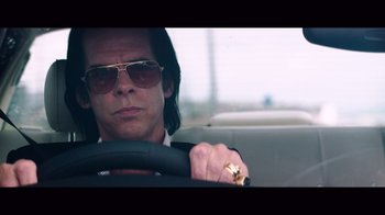 Movie still from “20,000 Days on Earth” (2014), directed by Iain Forsyth – A man driving a car wearing sunglasses and holding the steering wheel; Close Up shot, Low angle