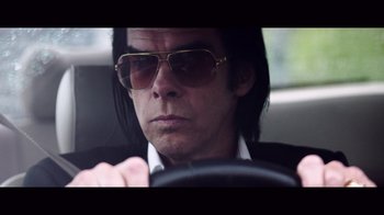 Movie still from “20,000 Days on Earth” (2014), directed by Iain Forsyth – A man wearing sunglasses sitting in the driver's seat of a car; Close Up shot, Low angle