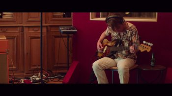 Movie still from “20,000 Days on Earth” (2014), directed by Iain Forsyth – A man sitting in front of an electric guitar in a room; Medium shot, Low angle