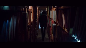 Movie still from “20,000 Days on Earth” (2014), directed by Iain Forsyth – A person walking down a library aisle with books; Medium shot, High angle