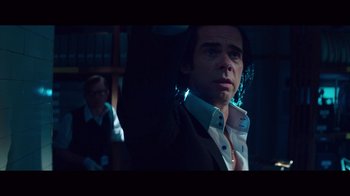 Movie still from “20,000 Days on Earth” (2014), directed by Iain Forsyth – A man in a suit and tie in a dark room; Medium shot, Over the shoulder angle