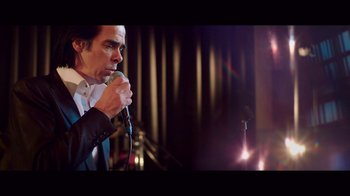 Movie still from “20,000 Days on Earth” (2014), directed by Iain Forsyth – A man holding a microphone in front of an audience; Medium shot, Over the shoulder angle