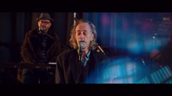 Movie still from “20,000 Days on Earth” (2014), directed by Iain Forsyth – A man with long hair is singing into a microphone; Medium shot, Low angle