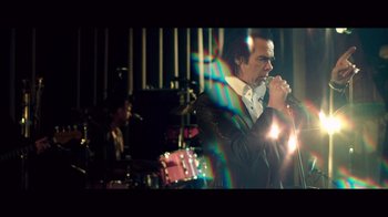 Movie still from “20,000 Days on Earth” (2014), directed by Iain Forsyth – A man is singing into a microphone in front of a band; Medium shot, Low angle
