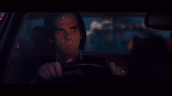 Movie still from “20,000 Days on Earth” (2014), directed by Iain Forsyth – A man sitting in the driver's seat of a car at night; Medium shot, Low angle