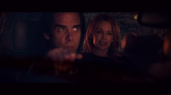 Movie still from “20,000 Days on Earth” (2014), directed by Iain Forsyth – A man and a woman sitting next to each other in front of a brick wall; Medium shot, Over the shoulder angle