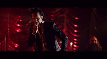Movie still from “20,000 Days on Earth” (2014), directed by Iain Forsyth – A man in a black jacket is singing into a microphone; Medium shot, Low angle
