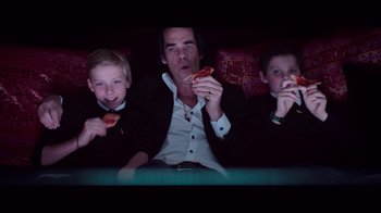 Movie still from “20,000 Days on Earth” (2014), directed by Iain Forsyth – A man sitting on a couch with two young boys; Medium shot, Overhead angle