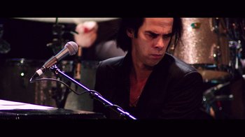 Movie still from “20,000 Days on Earth” (2014), directed by Iain Forsyth – A person sitting at a table with a microphone; Close Up shot, Low angle
