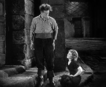 Movie still from “7th Heaven” (1927), directed by Frank Borzage – A man and a woman standing next to each other in front of a stone wall; Wide shot, High angle