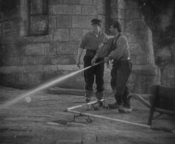 Movie still from “7th Heaven” (1927), directed by Frank Borzage – A black and white photo of two men with a fire hose; Wide shot, High angle