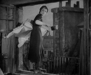 Movie still from “7th Heaven” (1927), directed by Frank Borzage – An old black and white photo of a woman holding a pan; Wide shot, Low angle