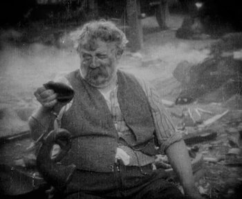 Movie still from “7th Heaven” (1927), directed by Frank Borzage – An old man sitting on the ground holding a cell phone; Medium shot, High angle