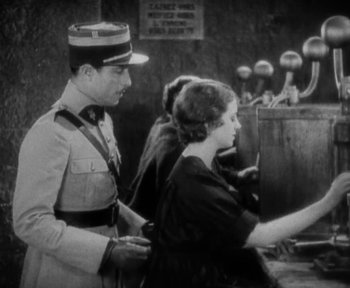 Movie still from “7th Heaven” (1927), directed by Frank Borzage – A man and a woman in uniform standing next to each other in front of a phone booth; Medium shot, Low angle