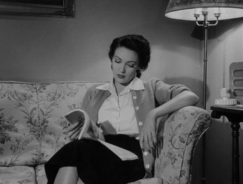 Movie still from “A Letter to Three Wives” (1949), directed by Joseph L. Mankiewicz – A black and white photo of a woman sitting on a couch reading; Medium shot, Low angle