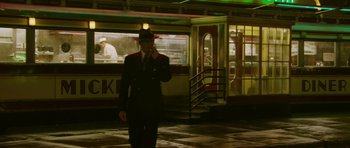 Movie still from “A Prairie Home Companion” (2006), directed by Robert Altman – A man in a suit and hat is standing in front of a building; Wide shot, Low angle