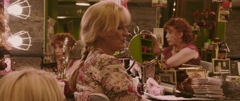 Movie still from “A Prairie Home Companion” (2006), directed by Robert Altman – A woman with long blonde hair sitting in front of a mirror; Medium shot, Over the shoulder angle