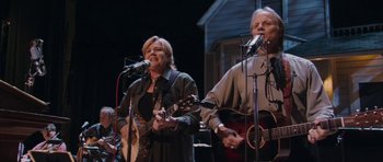 Movie still from “A Prairie Home Companion” (2006), directed by Robert Altman – A woman and a man playing guitar and singing on a stage; Medium shot, Low angle