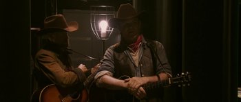 Movie still from “A Prairie Home Companion” (2006), directed by Robert Altman – A man in a cowboy hat is holding a guitar; Medium shot, Over the shoulder angle